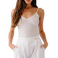 A woman wears the Sablyn Ada V-Neck Cami with Lace and high-waisted white pants, hands in her pockets, standing against a white background.