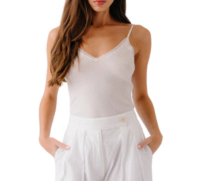A woman wears the Sablyn Ada V-Neck Cami with Lace and high-waisted white pants, hands in her pockets, standing against a white background.