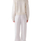 A woman, seen from the back against a white background, wears the Sablyn Sutton Slouchy Pullover in cream with ribbed detailing, paired with loose white pants and black high-heeled shoes.