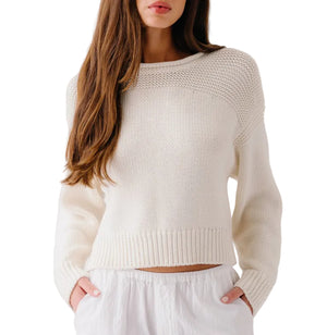 A woman with long brown hair wears the Sablyn Sutton Slouchy Pullover in white, paired with white pants, standing against a plain white background.