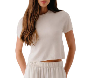 A woman with long brown hair wears the Sablyn Charleston Relaxed Crewneck Tee in beige, paired with matching elastic-waist pants, standing against a white background.