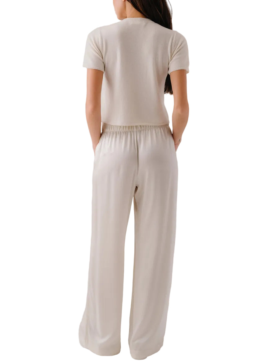 A woman stands with her back to the camera, wearing the Sablyn Charleston Relaxed Crewneck Tee in beige, paired with matching wide-leg pants featuring an elastic waistband.