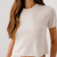 A woman wears the Sablyn Charleston Relaxed Crewneck Tee with light-colored pants, standing against a plain background.