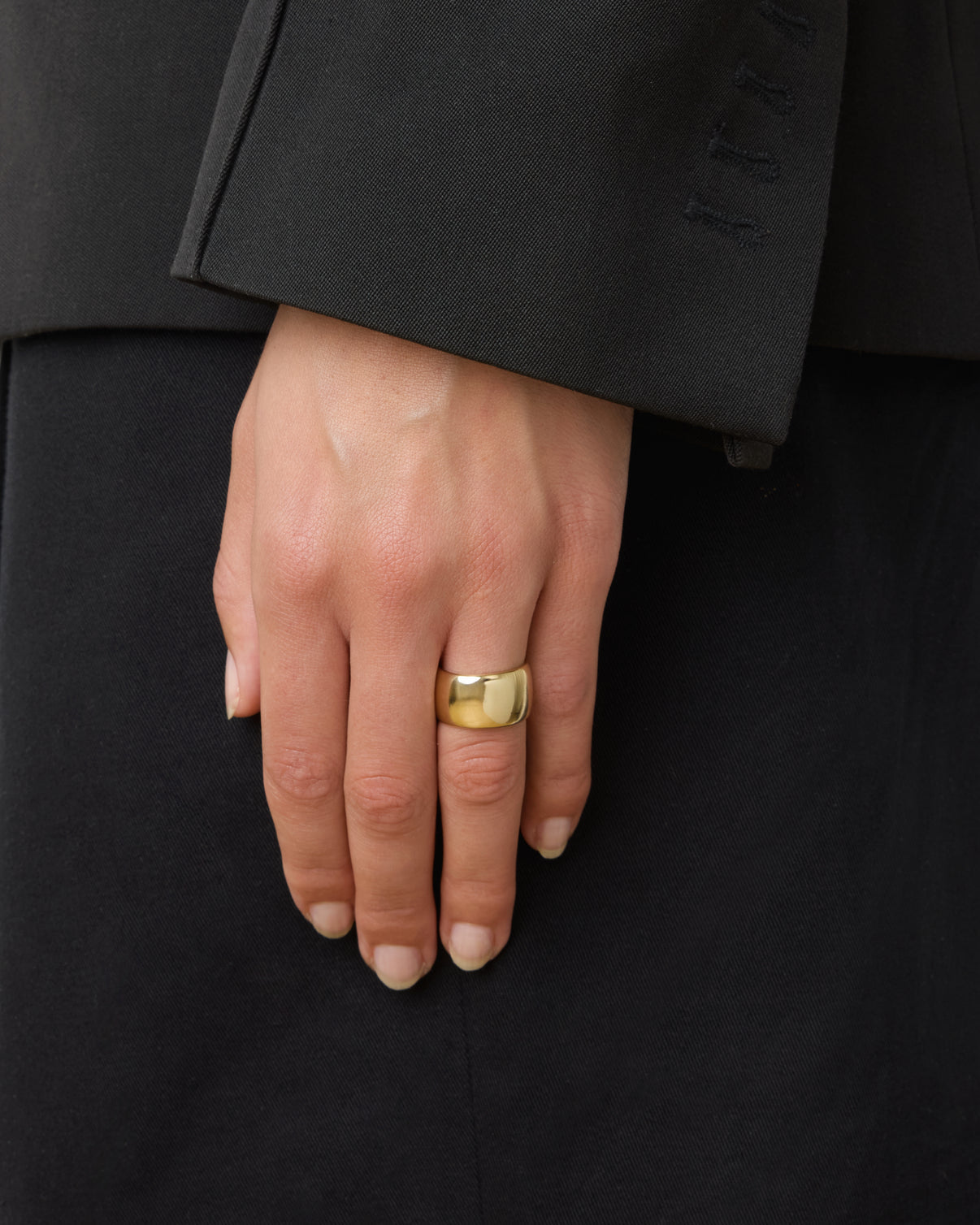 A hand wearing the Lie Studio Sandra Ring on the index finger, its sleek gold band adding elegance to a black suit.