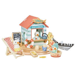 The Tender Leaf Sandy's Beach Hut by Tender Leaf Toys encourages imaginative play, featuring bird figurines, a wooden toy seagull, paper fish and chips, a deck chair, and a chalkboard menu. Ideal for kids who enjoy creative storytelling and igniting their imagination.