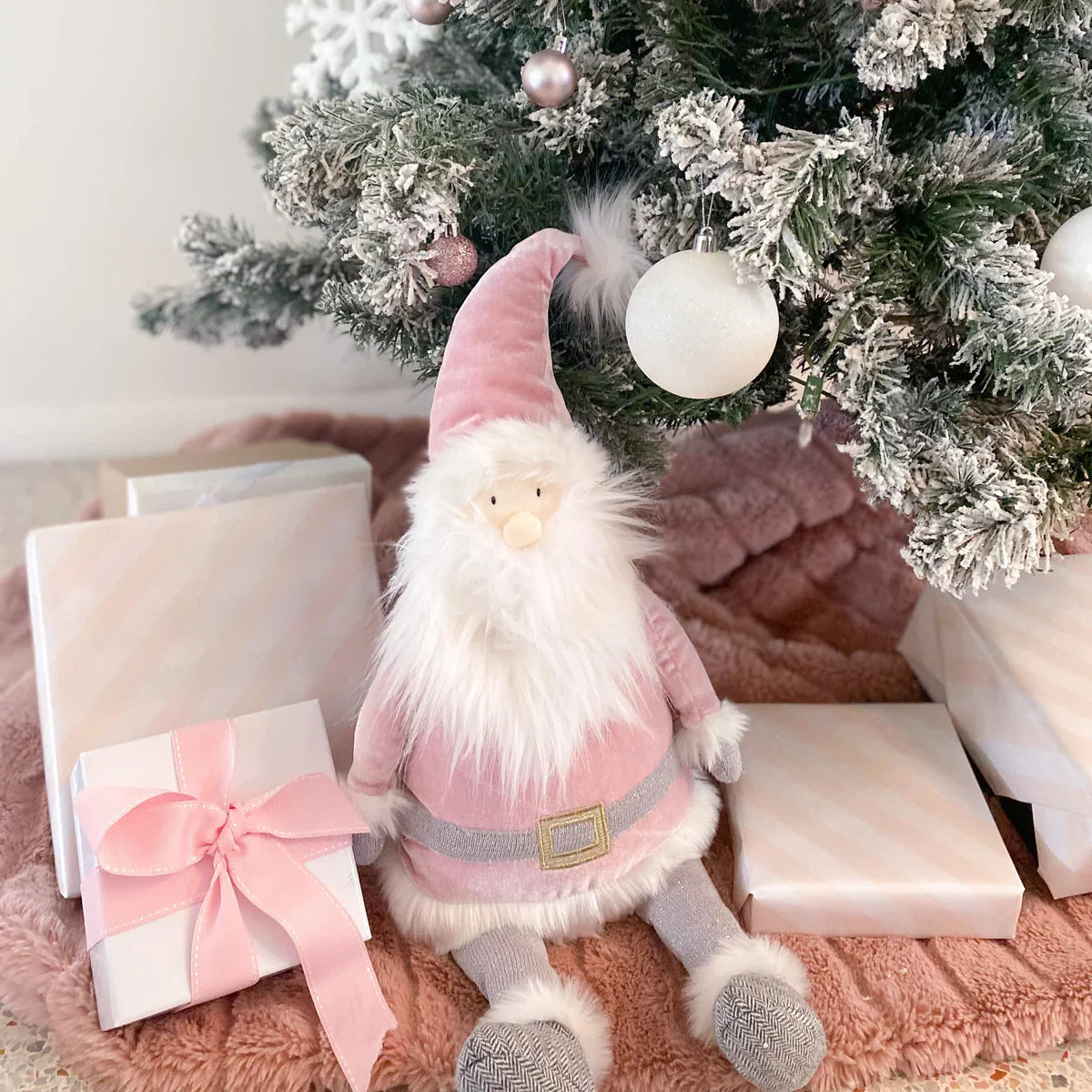 The MON AMI Santa Shelf Sitter in Dusty Rose, by Mon Ami, is comfortably seated under a Christmas tree surrounded by wrapped gifts adorned with pink ribbons, creating a delightful holiday accent for your Christmas decor.