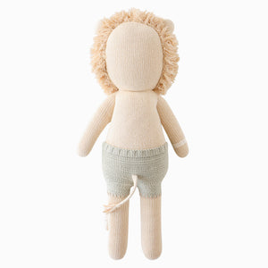 Sawyer the Lion - Little 13" by Cuddle + Kind, a stuffed lion toy with a fuzzy mane, beige body, and light green knitted shorts, shown from the back against a white background.