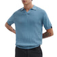 A man wearing a Rag & Bone Saxon Silk-Cotton Polo Shirt in light blue and black pants stands with his hands behind his back.