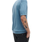 Wearing a Rag & Bone Saxon Silk-Cotton Polo Shirt and black pants, a person with several arm tattoos stands with one hand in their pocket.