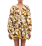 A person is wearing the Ulla Johnson Anita Dress, which features a long-sleeve design with a floral pattern in yellow, brown, and cream. It includes a flattering V-neck and a chic removable tie belt.