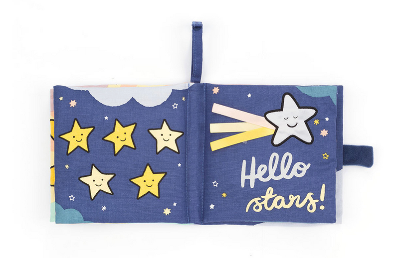 A colorful, interactive fabric children's book, the Jellycat Hello Moon Fabric Book by Jellycat, features a page with smiling yellow stars and another page with a shooting star and the text "Hello stars!" against a blue backdrop, perfect for baby exploration.