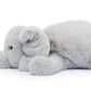 A Jellycat Wanderlust plush toy elephant, affectionately named Wanderlust Elly, lying down on its side with its trunk curled slightly and its legs extended. The toy is light grey and has a soft, fluffy texture that's perfect for any traveller's friend.