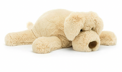 A large, light brown plush dog toy lies flat on its stomach with legs spread out and head resting on the ground, making the Jellycat Wanderlust by Jellycat the perfect chilled softie for any adventure.