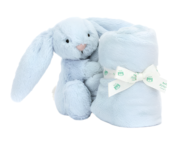 A Jellycat Bashful Blue Bunny Soother sits next to a rolled, light blue soft blanket secured with a white ribbon featuring small green bear designs. This delightful newborn gift is crafted from recycled fibers, making it both adorable and eco-friendly.