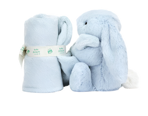 A Jellycat Bashful Blue Bunny Soother, made from recycled fibers, is seated beside a rolled-up matching light blue plush blanket tied with a ribbon labeled "Baby Blanket." The bunny has long ears and a white, fluffy tail, making it the perfect newborn gift.