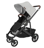 The UPPAbaby Cruz V2 Stroller by UPPAbaby features a modern design with a sleek black frame, four wheels, and a black toddler seat complemented by a light gray canopy. It includes an adjustable brown handlebar and a convenient storage basket underneath.