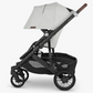 Side view of a black and gray UPPAbaby Cruz V2 Stroller with four wheels, a canopy, and an under-seat storage basket. The brand name "UPPAbaby" is visible on the side. It features an adjustable handlebar for added convenience.