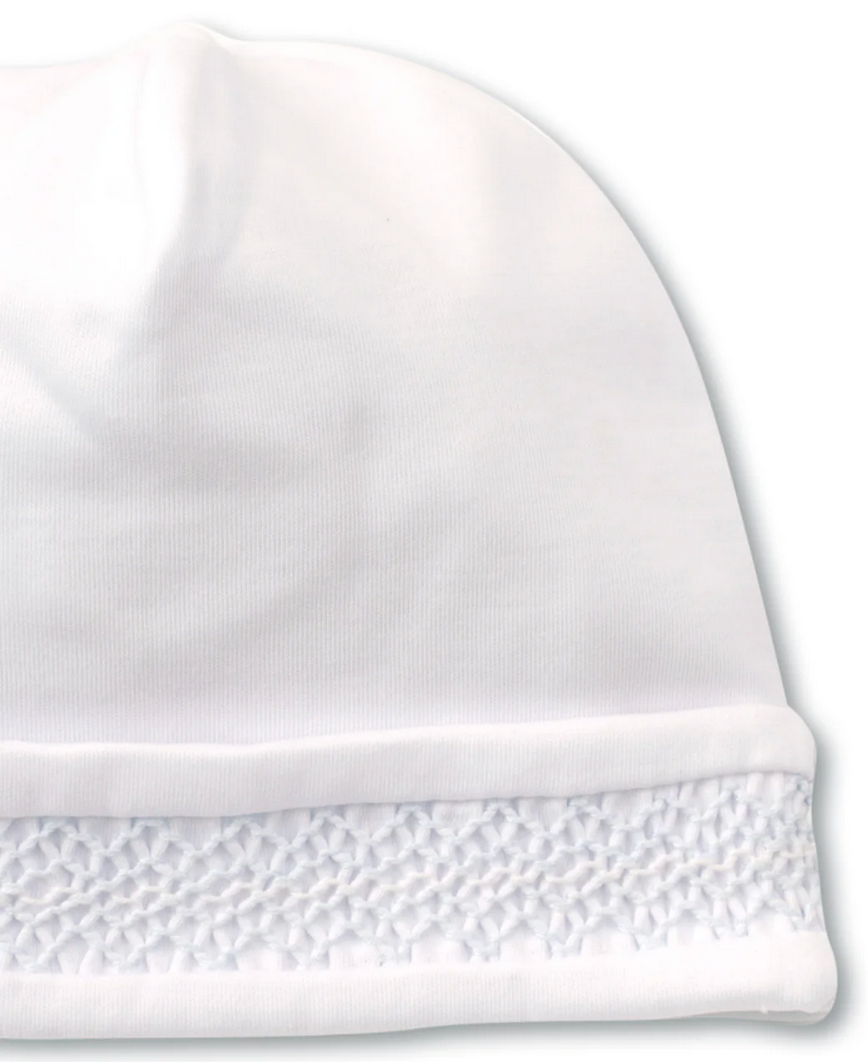 The Kissy Kissy Hat with Hand Smocking by Kissy Kissy is a white knit cap made from ultra-soft Peruvian cotton, showcasing an intricately textured woven detail near the bottom edge.