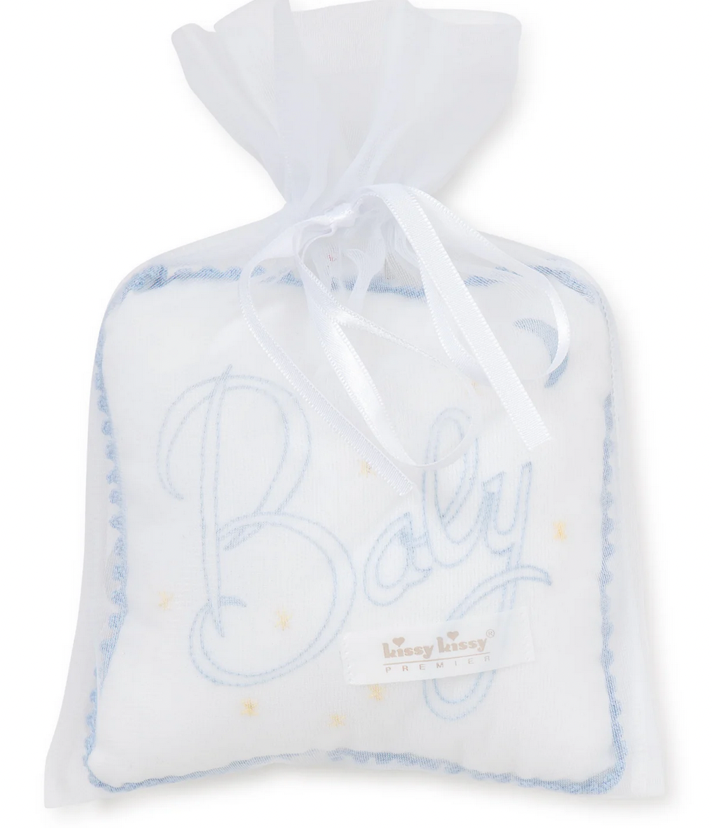 The Kissy Kissy Blue "Baby" Musical Pillow features a charming white sachet with a blue-stitched "Baby" design. It is elegantly trimmed with lace and tied with a white ribbon, making it an ideal baby gift. The delicate tulle bag adds an extra touch of charm.