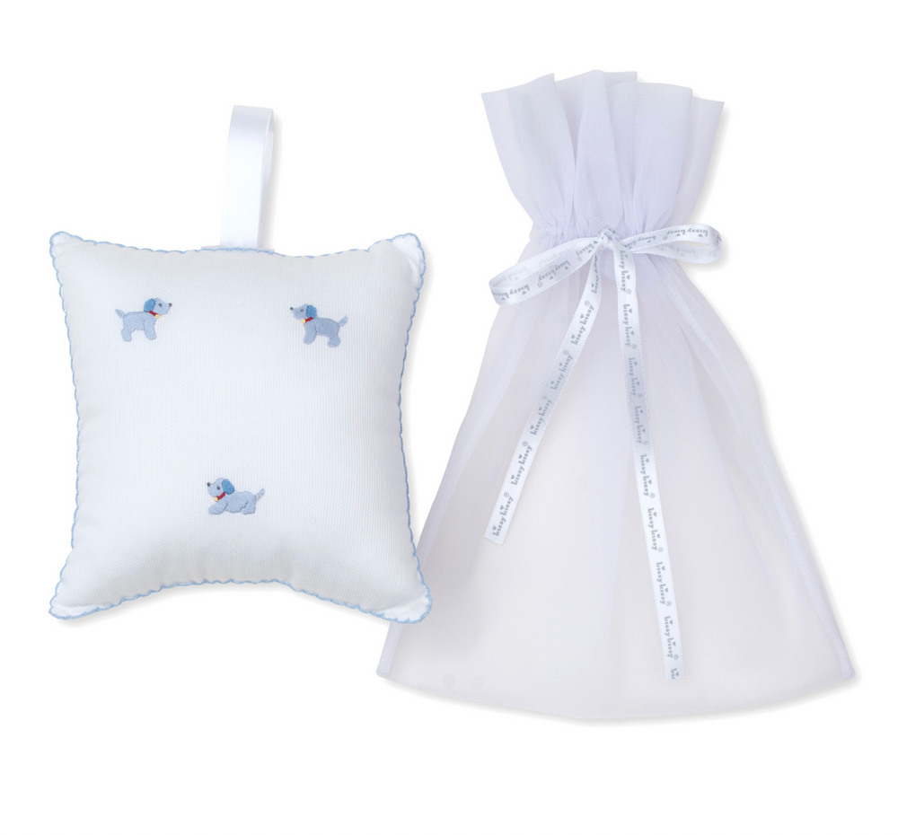 The Kissy Kissy Hand Embroidered Premier Puppies Musical Pillow with Tulle Bag in White/Light Blue features a small white pillow adorned with blue dog embroidery and intricate hand-embroidered detailing, complete with a hanging ribbon. It comes paired with a sheer white tulle bag secured by a ribbon tie, making it an ideal keepsake for puppy enthusiasts.