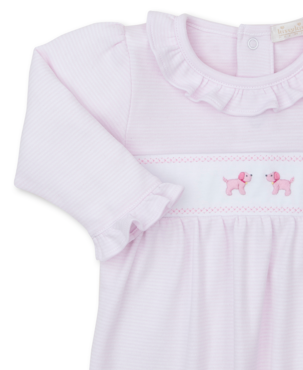 The Kissy Kissy Premier Hand Embroidered Puppies Playsuit by Kissy Kissy is a pink long-sleeve baby dress made from soft Pima cotton, featuring a ruffled collar and cuffs, and adorned with hand-embroidered pink poodles on the front.