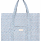 The Minnow Overnighter Tote by Minnow is a blue, floral-patterned, quilted fabric tote bag featuring two long straps and a square front pocket. A small label reading "minnow" is attached to the front pocket, adding a charming touch to your collection. Additionally, its spacious interior ensures you can carry all your essentials with ease.