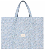 The Minnow Overnighter Tote by Minnow is a blue, floral-patterned, quilted fabric tote bag featuring two long straps and a square front pocket. A small label reading "minnow" is attached to the front pocket, adding a charming touch to your collection. Additionally, its spacious interior ensures you can carry all your essentials with ease.