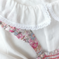 Close-up of the Tartine et Chocolat Ensemble Court Liberty Pink Overall Top Set, featuring a white garment with a ruffled collar. A pink floral-patterned fabric, likely Liberty cotton, peeks through the ruffles. The label reads "Tartine et Chocolat.