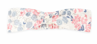 The Tartine et Chocolat Raspberry Printed Flowery Headband, a charming floral accessory from Tartine et Chocolat, showcases a delightful pattern of blue and pink flowers on a white background and is elegantly tied in a bow shape at the center to elevate your style.