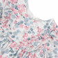 Close-up of the Tartine et Chocolat Rasberry Printed Flowery Dress for baby girls, featuring a charming floral pattern with pink and blue flowers. This dress has short sleeves and a white neckline adorned with lace trim, making it perfect for winter outfits. Crafted from high-quality fabric by Tartine et Chocolat, it ensures both comfort and durability.