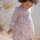 A young child with curly hair wears the Tartine et Chocolat Raspberry Printed Flowery Dress and looks down while walking outdoors.