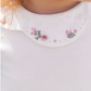 A close-up image of Tartine et Chocolat's Long Sleeve Onesie for children, showcasing a white shirt with a ruffled collar adorned with small pink and green embroidered flowers.