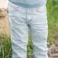 A toddler wearing the Tartine et Chocolat Sky Blue Striped Trousers stands outdoors near green grass and rocks, showcasing one of the many adorable outfits made from soft and comfortable fabric by Tartine et Chocolat.