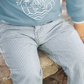 A child in an adorable outfit, featuring a light blue sweatshirt made of soft and comfortable fabric, paired with Tartine et Chocolat Sky Blue Striped Trousers for baby boys by Tartine et Chocolat, sits on a stone surface.