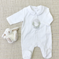 The Tartine et Chocolat Pyjama Snowball Bunny Onesie, made of 100% cotton with a snow globe design, laid on a beige textured background next to a small stuffed lamb toy. Perfect for newborn pajamas.