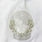 A close-up of the Tartine et Chocolat Pyjama Snowball Bunny Onesie shows a white 100% cotton fabric featuring an illustration of a larger and a smaller rabbit within a decorative circular frame, surrounded by stars and foliage, along with the text "Tartine et Chocolat" below. Perfect for newborn pajamas.