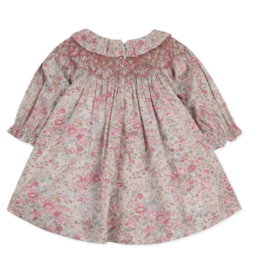 The Tartine et Chocolat Fabric Liberty Pink Dress from Tartine et Chocolat features a floral-patterned, long-sleeve design with smocked detailing on the chest and a round neckline. The light pink fabric is adorned with small multicolored flowers, reminiscent of Print Liberty.