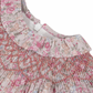 Close-up of the Tartine et Chocolat Fabric Liberty Pink Dress, showcasing a floral-patterned fabric with intricate smocking and ruffle details, featuring pink, beige, and blue flowers. This charming fabric is perfect for a newborn dress.