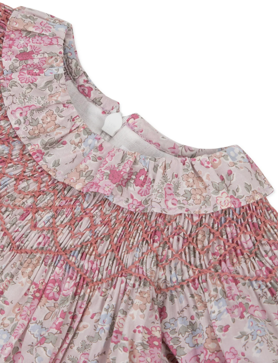 Close-up of the Tartine et Chocolat Fabric Liberty Pink Dress, showcasing a floral-patterned fabric with intricate smocking and ruffle details, featuring pink, beige, and blue flowers. This charming fabric is perfect for a newborn dress.