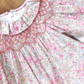 A close-up of the Tartine et Chocolat Fabric Liberty Pink Dress from Tartine et Chocolat, featuring intricate smocked detailing around the collar and chest area, and showcasing a beautiful Print Liberty floral pattern with pink and beige flowers on a light fabric.