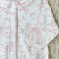 A close-up of the Tartine et Chocolat Pale Pink Toile Pyjama, featuring a white onesie adorned with pale pink floral patterns and a Peter Pan collar, lying on a beige textured surface—perfectly capturing the soft and comfortable fabric ideal for baby girl pajamas from the renowned brand, Tartine et Chocolat.