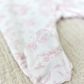 Close-up of a baby girl's foot covered by the Tartine et Chocolat Pale Pink Toile Pyjama, lying on a textured beige surface.