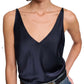 A woman wears the Sense of Shine Tank by Dorothee Schumacher—a dark navy stretch silk-satin V-neck camisole with adjustable spaghetti straps—paired with blue jeans and a black belt featuring a decorative gold buckle.