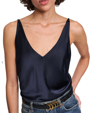 A woman wears the Sense of Shine Tank by Dorothee Schumacher—a dark navy stretch silk-satin V-neck camisole with adjustable spaghetti straps—paired with blue jeans and a black belt featuring a decorative gold buckle.
