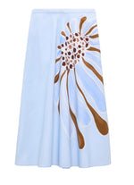 The Floral Power Skirt by Dorothee Schumacher is a light blue cotton poplin midi-skirt with a fitted waist and a bold abstract brown and white floral design on one side.