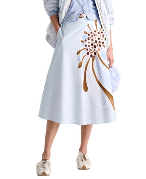 A person wears the Dorothee Schumacher Floral Power Skirt, a light blue cotton poplin midi with bold brown and white print, styled with a fitted-waist light blue shirt, jacket, and white shoes.