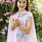 A young girl shines outdoors in the Great Pretenders Pink Sequins Twirl Cape, pairing it with a pastel butterfly purse—an enchanting addition to any children’s costume accessory collection.