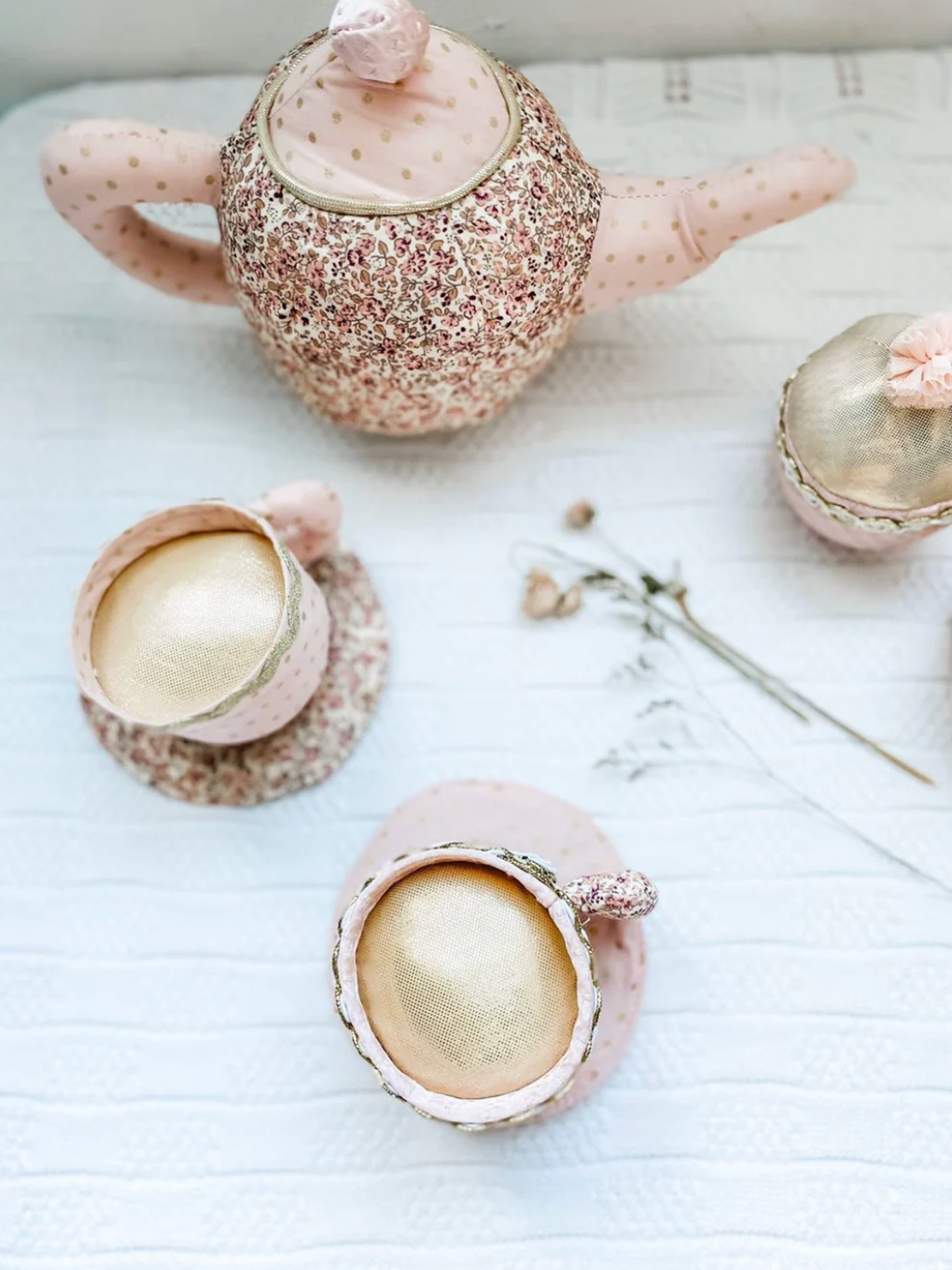 The Mon Ami Floral Stuffed Toy Tea Set, featuring two matching teacups and a sugar bowl, is displayed on a white textured surface with dried flowers beside it.