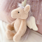 The MON AMI Luna Unicorn Fairy, a plush toy from Mon Ami featuring a horn and wings, sitting against pink tulle fabric adorned with gold stars, is the perfect gift for toddlers.