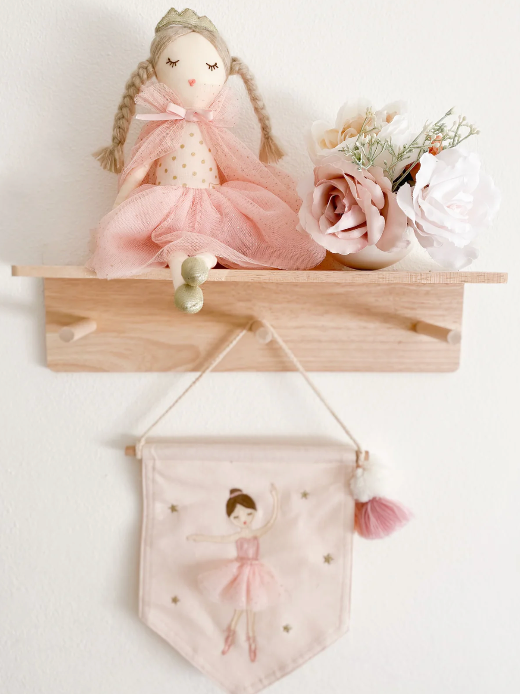 A Mon Ami Madeline Princess Doll sits on a wooden shelf next to a small vase of artificial flowers, with a pink ballerina banner hanging beneath the shelf.